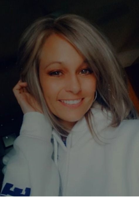 Smiling person with long hair wearing a white hoodie, posing indoors.