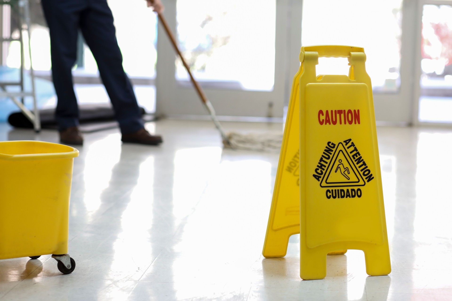 Senior Adult Janitor mops floor at entry to offices.